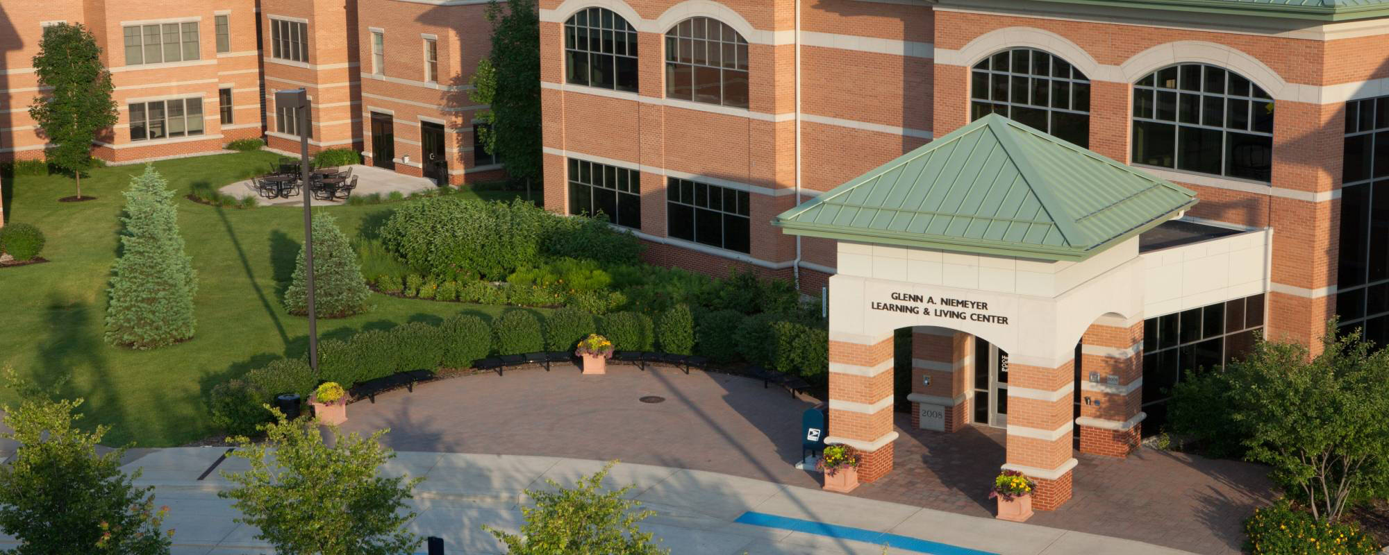 Brick building with green roof, Niemeyer East & West Apartments, surrounded by lush landscaping and trees, creating a peaceful, academic atmosphere.